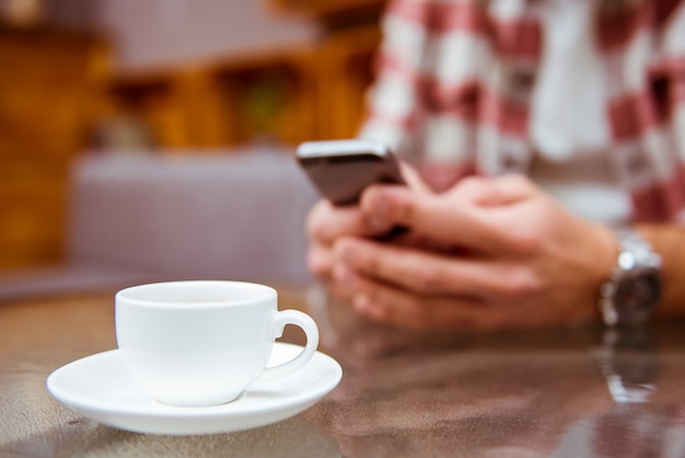 Las manos de los hombres miran algo en el teléfono inteligente y beben café.