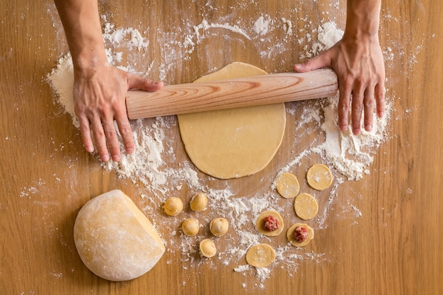 Manos de hombres rodando la masa para la preparación de albóndigas de carne en la mesa de madera.