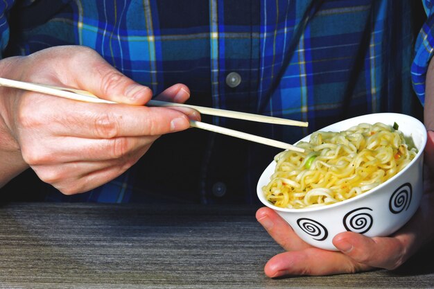 Las manos de los hombres sostienen los fideos con palillos. Fideos chinos, palos, manos.