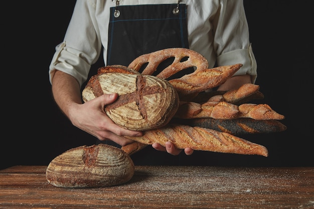 Las manos de los hombres sostienen muchos panes diferentes en una mesa de madera.