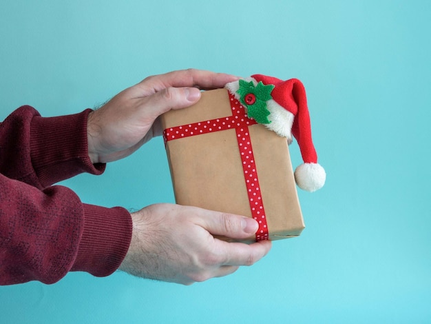 Las manos de los hombres sostienen un regalo con un lazo rojo y una cinta de raso en la mano sobre uno azul