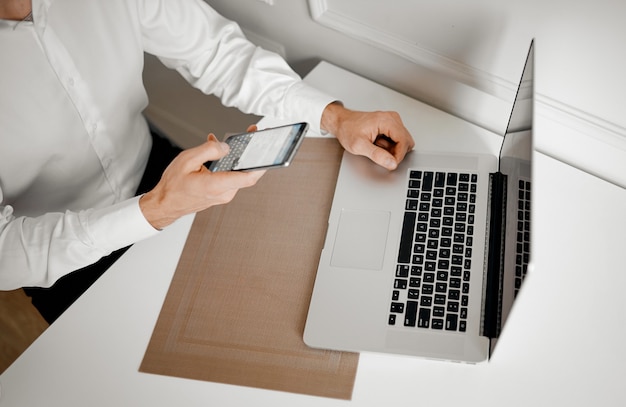 Las manos de los hombres sostienen el teléfono inteligente junto a la computadora portátil