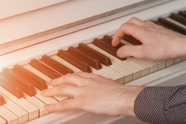 Manos de los hombres en el teclado del piano con luz solar.