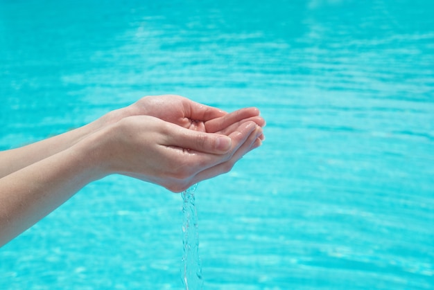 Manos humanas con agua clara sobre el fondo azul.