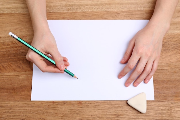 Manos humanas con lápiz escribiendo sobre papel y borrar goma sobre fondo de mesa de madera