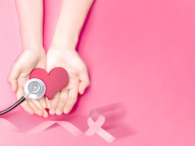 Manos humanas que muestran un corazón rosa y un estetoscopio con una cinta rosa