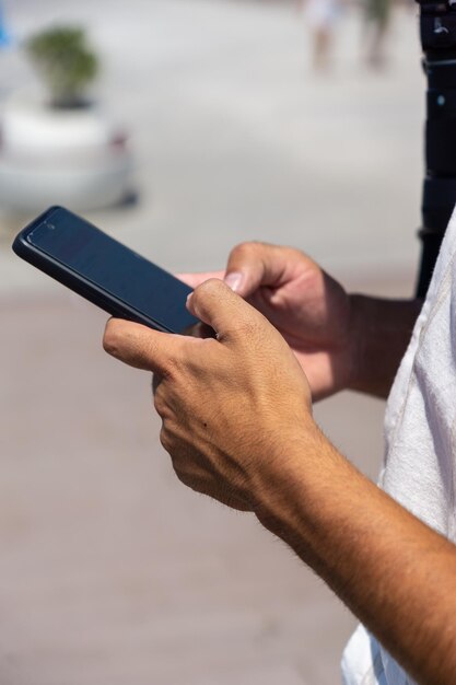 Manos irreconocibles de un joven usando un celular en la calle