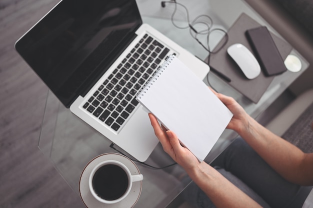 Manos irreconocibles de la mujer que escriben en la computadora y el cuaderno vacíos. Freelancer con teléfono inteligente y computadora portátil en casa durante la cuarentena. Marketing en Internet, finanzas, negocios, concepto de trabajo remoto