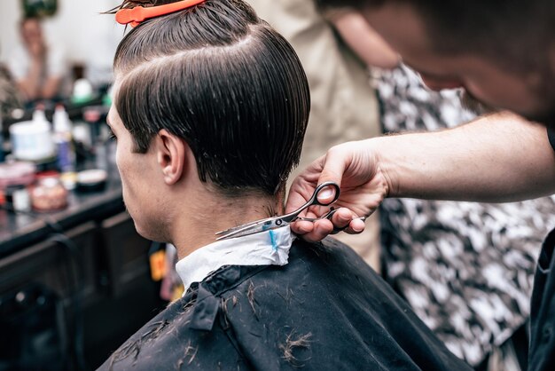 Las manos del joven barbero haciendo corte de pelo a hombre atractivo en peluquería