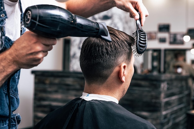 Las manos del joven barbero haciendo corte de pelo a hombre atractivo en peluquería