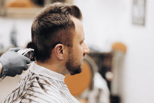 Foto las manos del joven barbero haciendo corte de pelo a hombre atractivo en peluquería