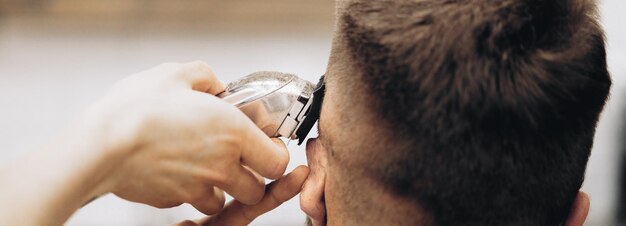 Las manos del joven barbero haciendo corte de pelo a hombre atractivo en peluquería