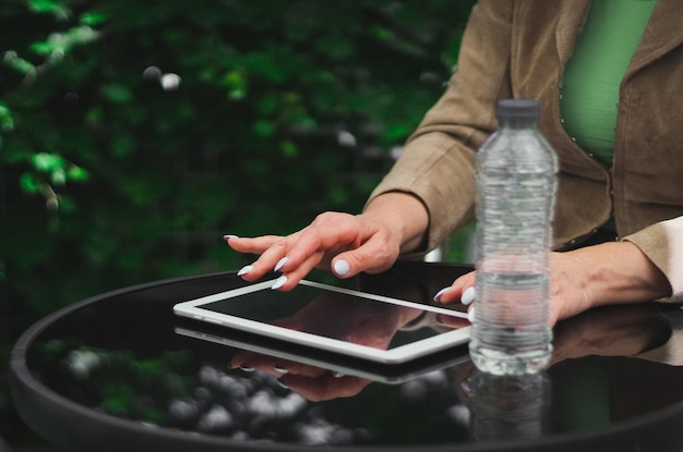 Foto las manos de una joven caucásica escribiendo en la pantalla negra de la tableta mientras está sentada en una mesa