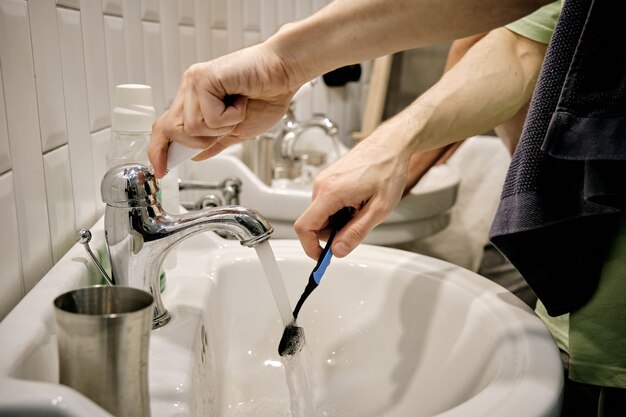 Manos de joven con cepillo de dientes sobre el lavabo en el baño.