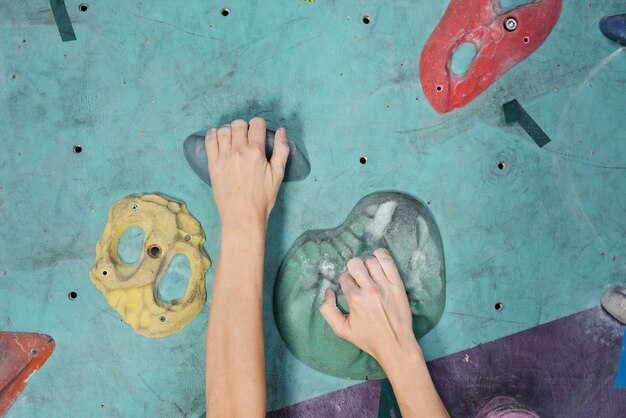 Manos de joven deportista agarrando rocas artificiales mientras alcanza el punto superior del equipo de escalada durante el entrenamiento