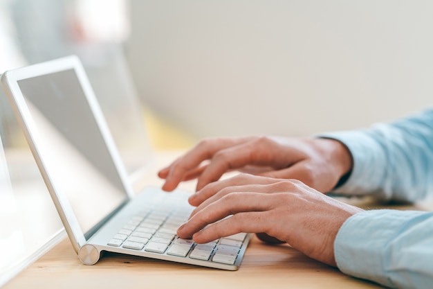 Manos del joven diseñador de sitios web tocando las teclas del teclado mientras trabaja frente al panel táctil en el lugar de trabajo en la oficina