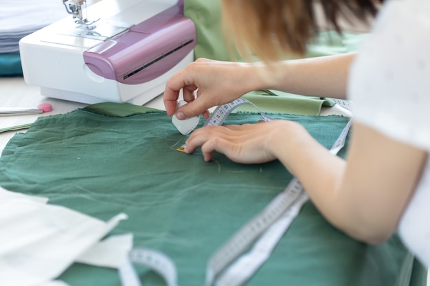 Las manos de una joven diseñadora hacen marcas para un nuevo producto de costura sentado en la mesa junto a la máquina de coser. Concepto de diseño y negocios creativos.