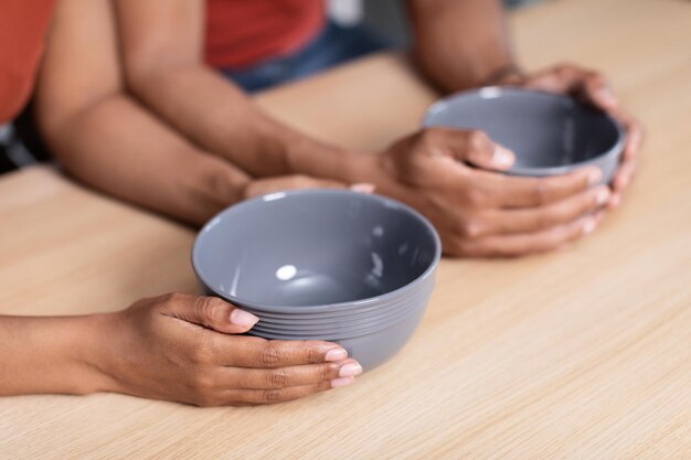 Manos de una joven esposa y esposo afroamericanos hambrientos sosteniendo platos vacíos en la mesa de la cocina