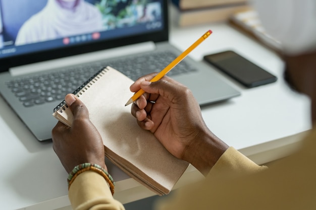 Manos de joven estudiante africano con lápiz sobre el Bloc de notas