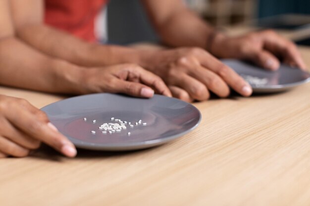 Manos de una joven familia negra sostienen platos con algunos granos de arroz en la mesa en la cocina recortada