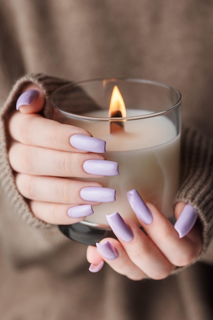Las manos de una joven con una hermosa manicura violeta claro sostienen una vela