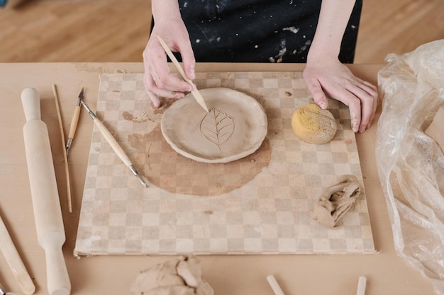 Manos de joven mujer creativa con herramienta de madera cortando adornos de hojas