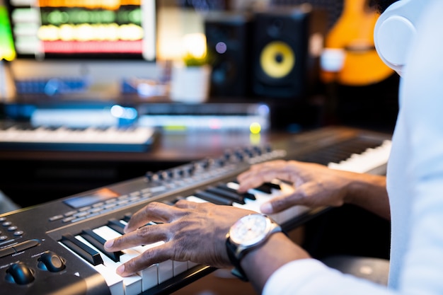 Manos de joven músico afroamericano sobre teclas de pianoboard trabajando solo en estudio de grabación de sonido contemporáneo