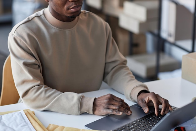 Manos de un joven negro con sudadera gris escribiendo en el teclado de una laptop