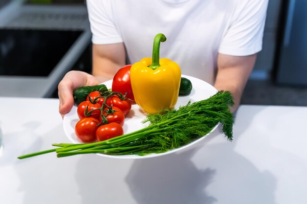 Las manos de un joven que sostiene un plato de verduras frescas.