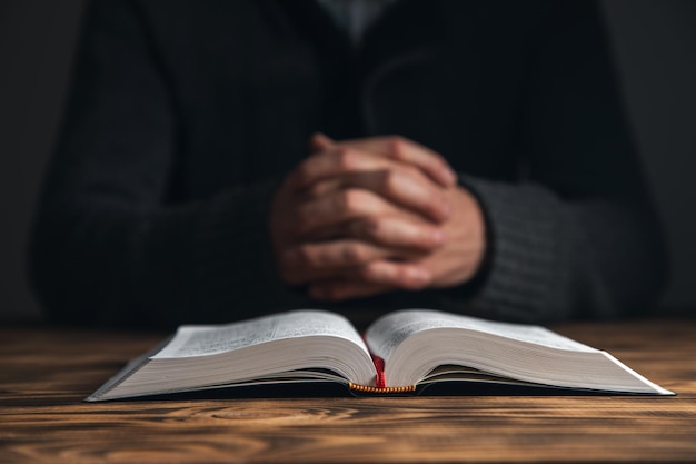 Manos de un joven rezando y de la Biblia sobre un fondo de escritorio de madera