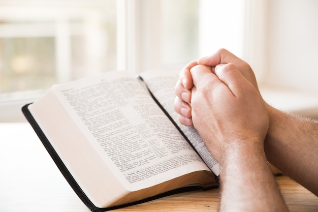 Manos juntas en oración sobre una Santa Biblia en concepto de iglesia para la fe, la espiritualidad y la religión