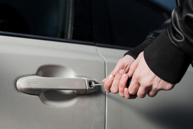 Manos de ladrón masculino tratando de abrir la puerta del coche con un destornillador. Vehículo de desbloqueo de Carjacker. Peligro de robo de auto