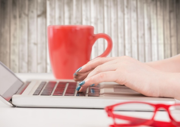 Manos con laptop y taza de café roja contra panel de madera borrosa