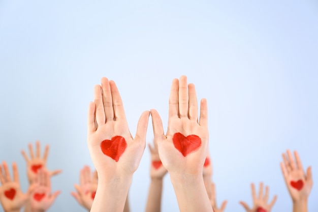 Manos levantadas en el aire con corazones dibujados en las palmas contra la luz.