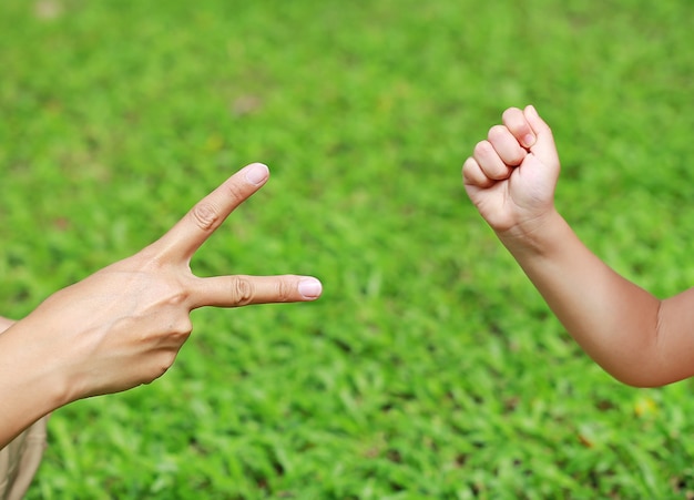 Manos de madre e hija, tijeras y roca - manos sobre fondo de hierba verde