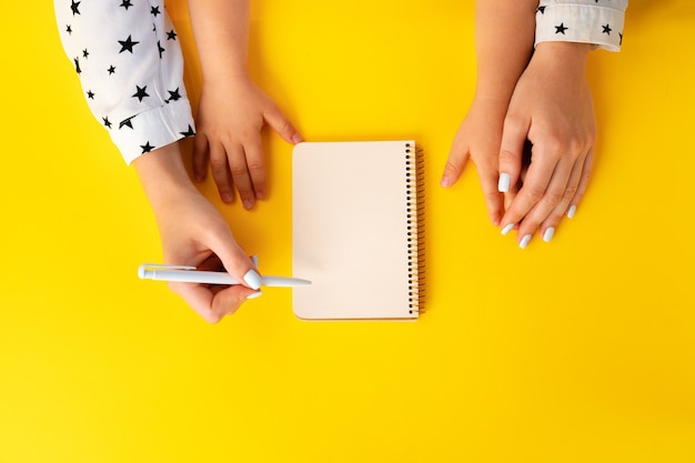 Manos de madre e hijo escribiendo en un bloc de notas, vista superior