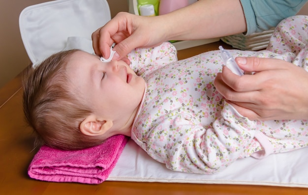 Manos de la madre limpiando los ojos del bebé con suero fisiológico en un algodón
