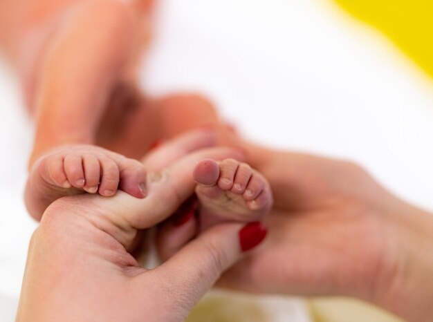 Manos de la madre sosteniendo los pies del recién nacido con amor Pequeñas líneas y arrugas en los pies tiernos Lindos y diminutos pies de bebé en la mano de los padres en un hogar acogedor