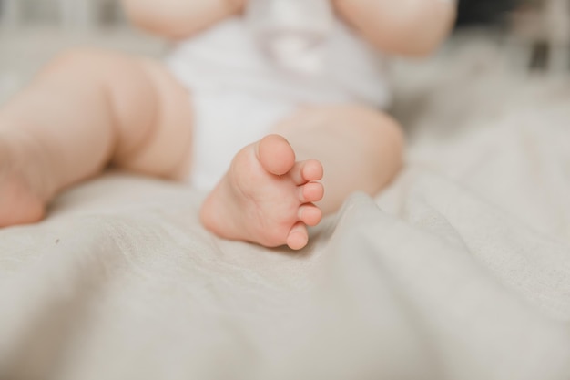 Las manos de la madre sostienen las piernas del bebé en una cama de algodón higiene y cuidado y cuidado del talón del recién nacido