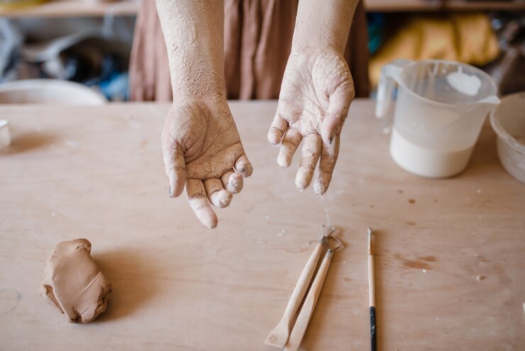 Foto manos maestras femeninas cubiertas con arcilla seca, interior del taller de alfarería