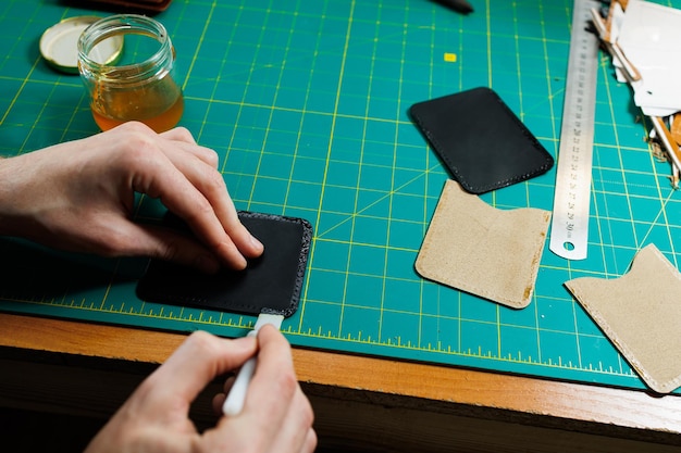 Las manos del maestro cosen productos de cuero hechos a mano Las manos de los hombres conectan las piezas creando accesorios de cuero de calidad Proceso de trabajo en un taller de cuero