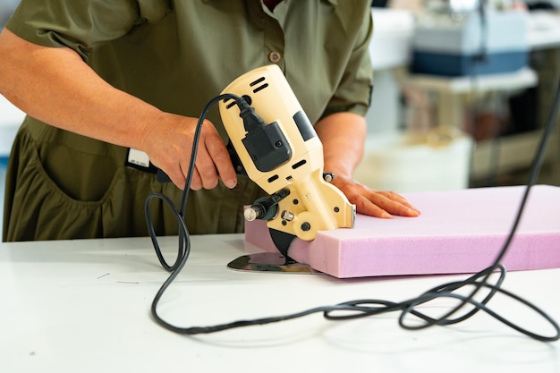 Las manos de un maestro de muebles cortan una pieza de espuma con una máquina de corte de espuma