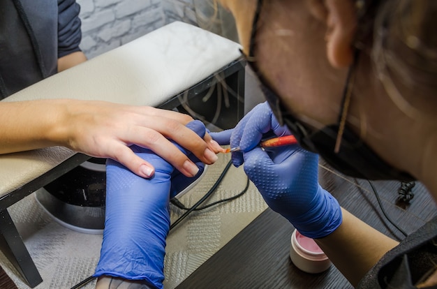 las manos del maestro pintan las uñas del cliente en el salón de manicura