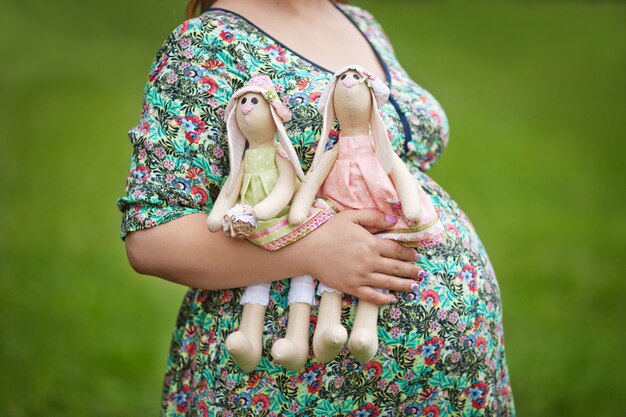 Manos de mamá sosteniendo dos conejos. Vientre de mujer embarazada. Gemelos