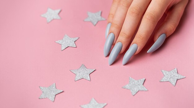 Manos con manicura gris sobre fondo rosa con estrellas plateadas