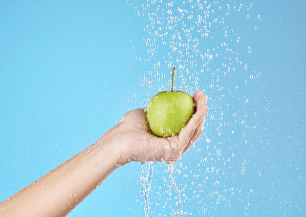 Manos de manzana verde y salpicaduras de agua para un estilo de vida saludable dieta vegana y nutrición en el fondo azul del estudio Palma sosteniendo frutas bajo agua corriente limpia para un refrigerio de desintoxicación de bienestar y vitaminas