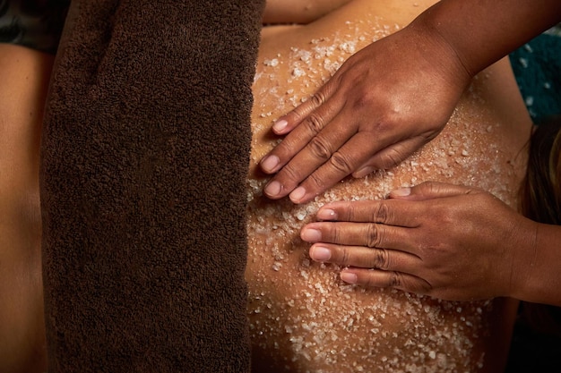 Las manos de la masajista aplican sal en la espalda de la mujer en el salón de spa