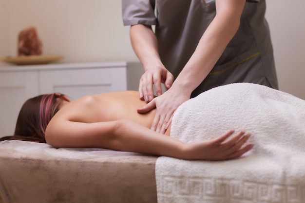 Manos de masajista de primer plano vertiendo aceite de masaje en la espalda femenina preparándose para un masaje relajante o revitalizante.