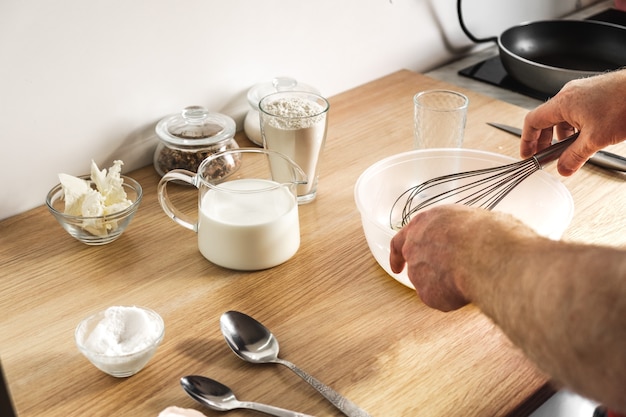 Manos masculinas amasan la masa con un batidor en un plato