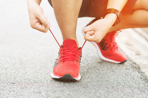 Manos masculinas del atleta atar cordones de los zapatos antes de la práctica. Corredor preparándose para el entrenamiento. Concepto de estilo de vida activo deportivo.